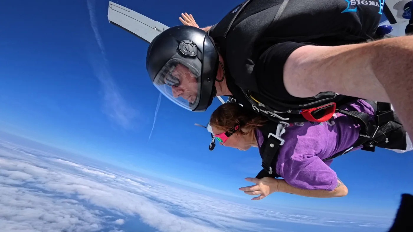 A freefall frame after ActionCut’s automatic grade: a tandem pair and camera flyer above the clouds